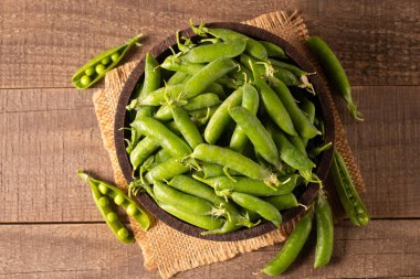 Tahta masadaki bir kasede taze bezelye ve kabuklar. Sebzeli sağlıklı yiyecek..  