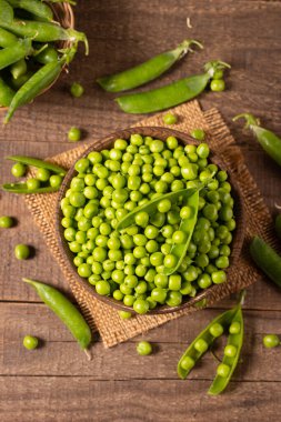Tahta masadaki bir kasede taze bezelye ve kabuklar. Sebzeli sağlıklı yiyecek..  