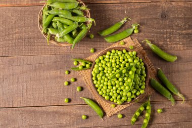 Tahta masadaki bir kasede taze bezelye ve kabuklar. Sebzeli sağlıklı yiyecek..  