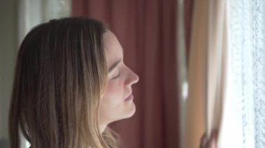 Uykulu yorgun kız sabahları pencereden dışarı bakarken esniyor, kapat.