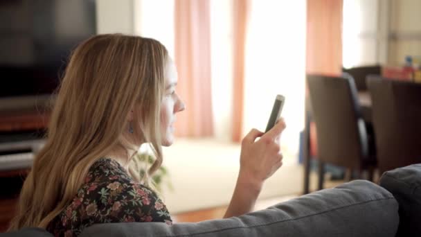 Kvinna sitter i vardagsrummet rullar på smarttelefon, blir arg och kastar telefon — Stockvideo