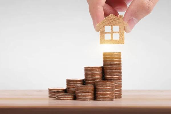 Pequeñas casas en la mano de pie sobre pilas de monedas — Foto de Stock