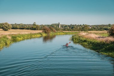 Woodford, Northamptonshire, İngiltere - 2 Eylül 2018. Parlak güneşli bir günde Northamptonshire'deki / daki Woodford kilit Denford kilise uzakta ile yakınındaki sakin bir nehir Nene boyunca iki canoeists çift kişilik bir kayık kürek