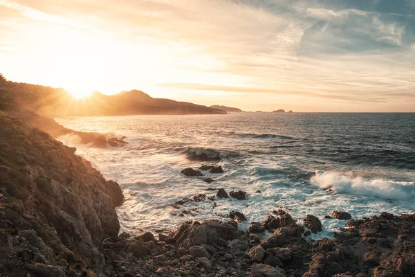 荒れた海と遠くにイルルッス Balagne 地域コルシカ島の岩だらけの海岸に沈む夕日 — ストック写真