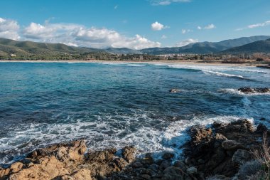 Dalgalar Corsica Balagne bölgede kar ile Lozari sahilde kayalık sahil şeridi üzerine yıkama mesafe dağlarda şapkalı