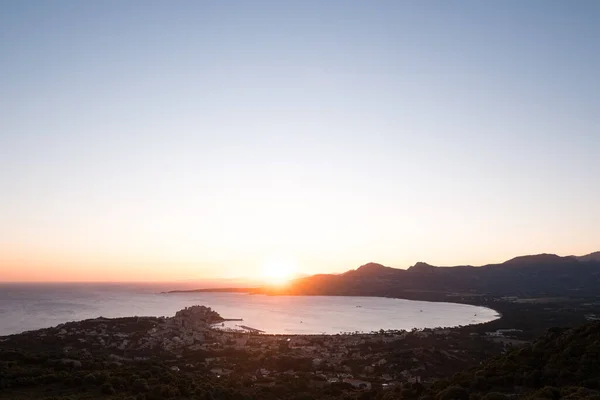 コルシカ島のバルーン地方のカルヴィの湾と要塞を照らす遠くの山々の上に昇る太陽 — ストック写真
