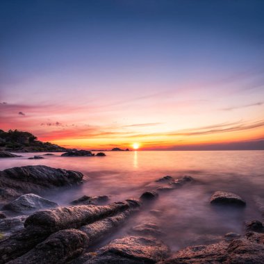 Güneş, Ile Rousse 'un kırmızı kayası La Pietra' nın üzerinde batıyor. Korsika 'nın Balagne bölgesinde. Ön planda kayalık bir kıyı şeridi var.