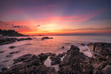 La Pietra üzerinde gün batımından sonra, Ile Rousse 'un kırmızı kayası, Korsika' nın Balagne bölgesinde, ön planda kayalık bir kıyı şeridi ile