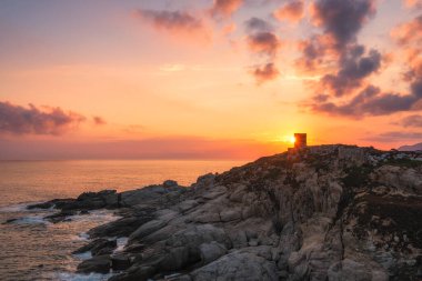 Lumio yakınlarındaki Punta Spano 'daki siluetli Ceneviz kulesinin üzerinde gün doğumu ve Korsika' nın Balagne bölgesinin kayalık kıyı şeridi. Uzakta Kaptan Corse ve ön planda Deniz İncirleri var.