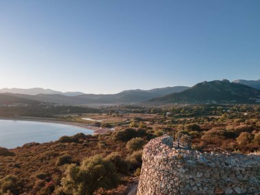Korsika 'nın batı kıyısındaki Losari kulesinin tepesindeki Losari plajı ve uzak dağlarıyla sabah güneşinin hava görüntüsü.