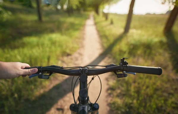 man riding a bike. holding bike handlebar with one hand. summertime outdoor leisure sport activity. first-person view bicycle riding