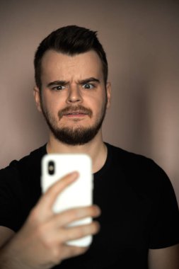 Sakallı üzgün adam telefonunu evde kullanıyor.