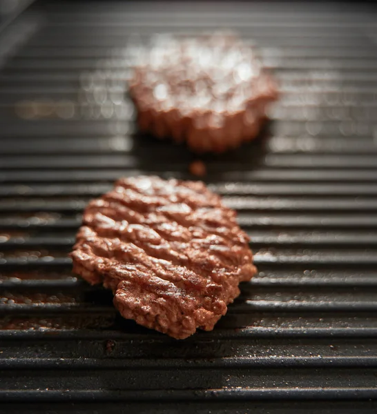 ground meat burger patties on griddle pan cooking. Dark background Grille