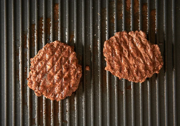 ground meat burger patties on griddle pan cooking. Dark background Grille