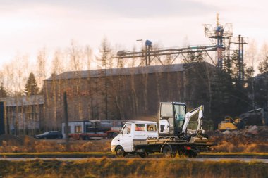 Sarı kamyon inşaat alanında kazıcı taşıyor.