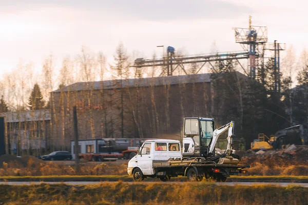 Sarı kamyon inşaat alanında kazıcı taşıyor.