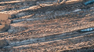 Çamurlu su birikintileri ve lastik izleri toprak yolda engebeli bir arazi oluşturuyor.