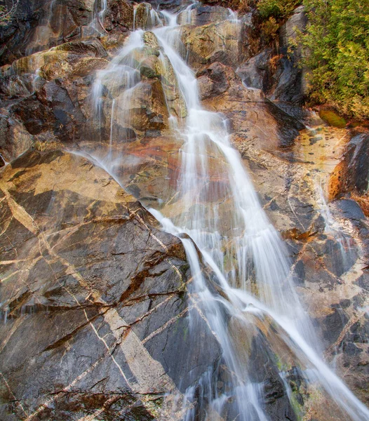 絹のような水がカラフルな岩の層の上を流れ 石のパターンが印象的です — ストック写真