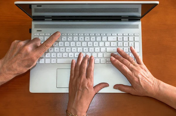 Top view of hands of old people using a laptop and pointing the computer screen. Elderly people and technology. Couple using a computer.