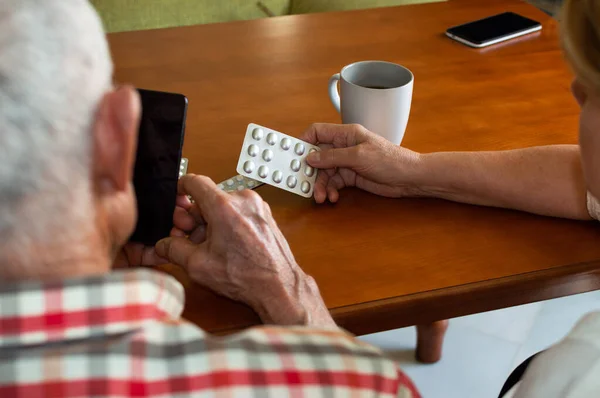 Elderly couple consulting medical questions online using the phone at home. Old people using technology to find information about medications.