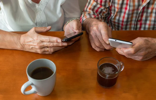 Yaşlı insanların evde akıllı telefon kullanırken sıcak içeceklerin keyfini çıkardıkları en iyi manzara. Yaşlılar ve teknoloji kavramı.