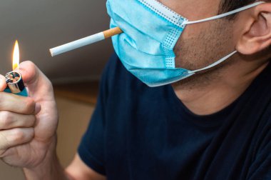 Maskeli genç adam sigara yakıyor. Coronavirus komik bir kavram