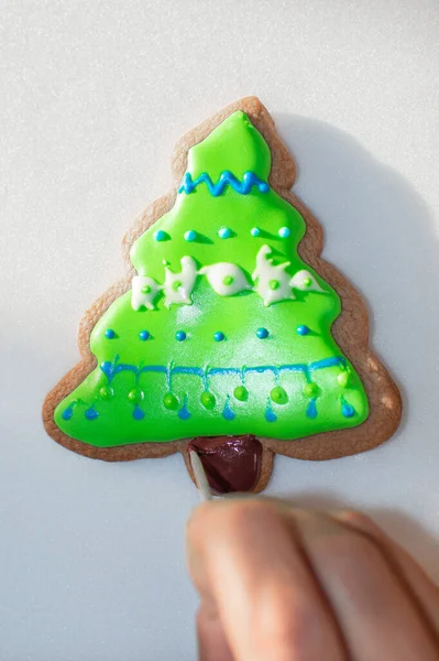 Top view of hand decorating a homemade cookie with colorful glaze. Cooking at home, painting a tree with glaze and colorant.