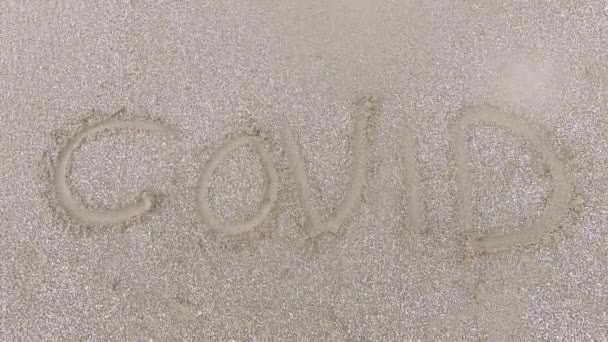 海岸でのコロナウイルスのパンデミックの終わりについての概念 ビーチの砂の中に書かれた単語 Covid を消去 — ストック動画