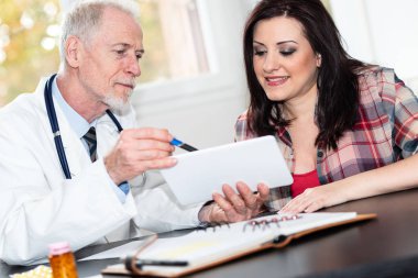 Kıdemli doktor raporları dijital tablet üzerinde kadın hastaya gösterilen.
