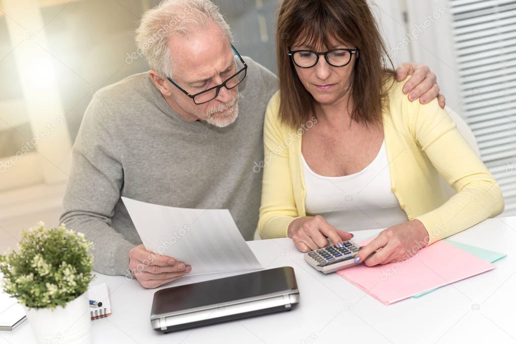 Senior couple checking financial document at home, light effect