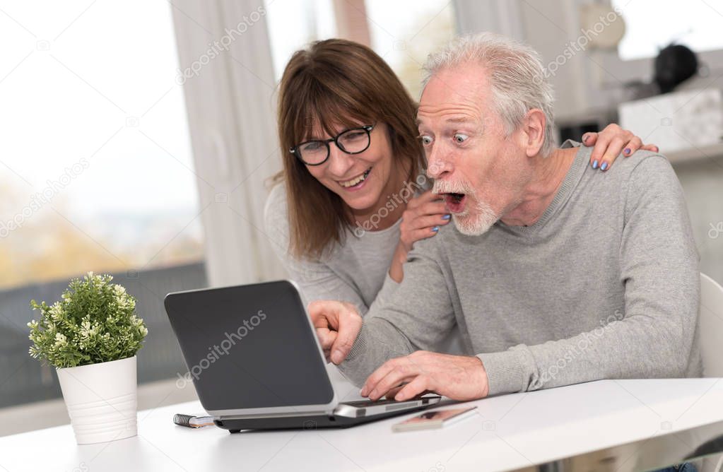Happy mature couple having an amazing surprise on laptop