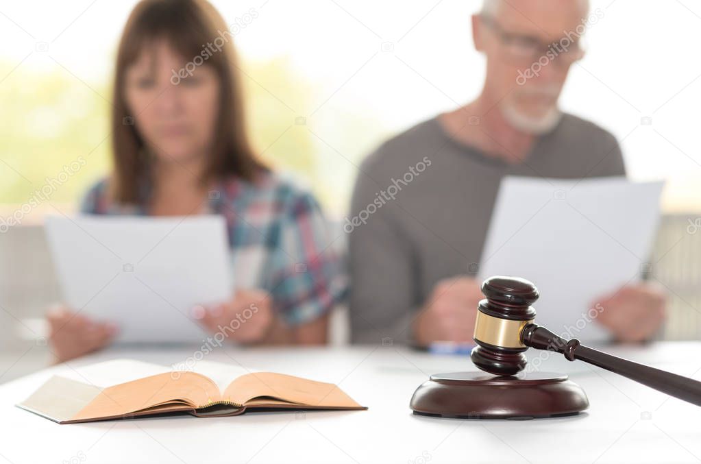 Divorce concept with judge gavel and couple reading documents in background, focus on foreground