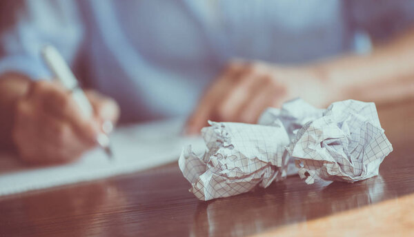 Person writing on notebook with crumpled sheet on table, focus on foreground