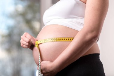 Hamile bir kadın karnını mezurayla ölçüyor.