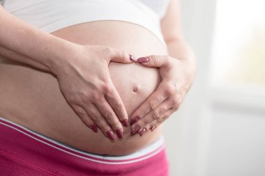 Hamile kadının karnı üzerinde bir kalp şeklinde elele