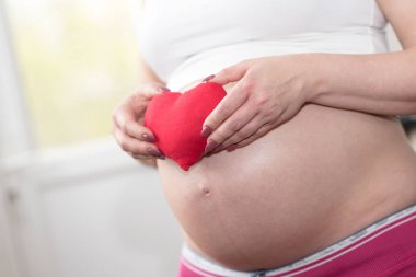 Karnının önünde kırmızı bir kalp tutan hamile kadın