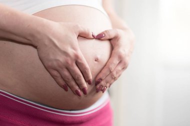 Hamile kadının karnı üzerinde bir kalp şeklinde elele