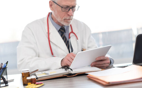 Male senior doctor using digital tablet