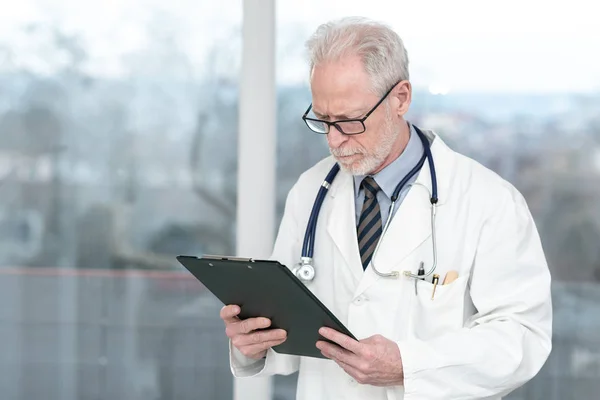 Старший врач читает заметки на планшете — стоковое фото