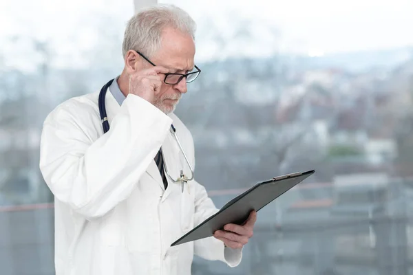 Senior doctor reading notes on clipboard — Stock Photo, Image