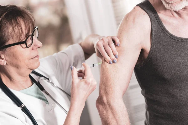 Médico femenino inyectando la vacuna a un paciente mayor —  Fotos de Stock