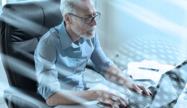 Dizüstü bilgisayarda çalışan kıdemli işadamının portresi, parlak ışık;