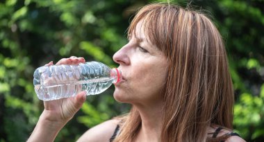 Şişeden su içen olgun bir kadın.