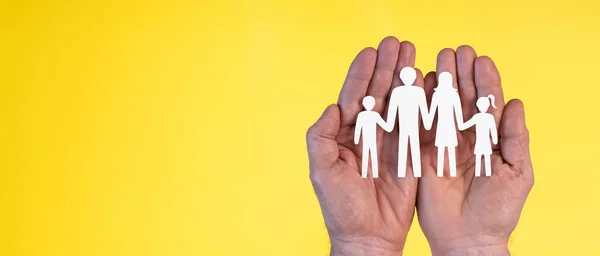 Concept of family insurance with paper family in hands on yellow background
