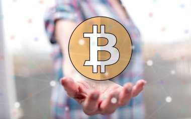 Bitcoin kavramı arka plandaki bir kadının elinin üstünde.
