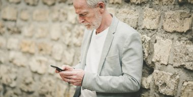 Olgun bir adam cep telefonunu açık havada kullanıyor.