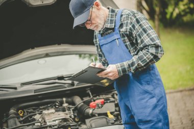 Araba tamircisi bir araba motorunu kontrol ediyor ve panoya yazı yazıyor.