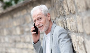 Olgun bir adam cep telefonunu açık havada kullanıyor.