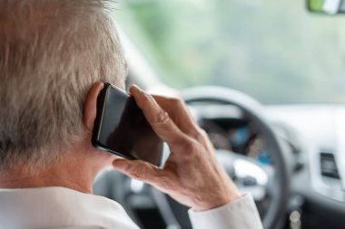 Adam araba sürerken cep telefonuyla konuşuyor.