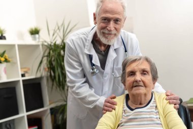 Erkek doktor huzurevindeki yaşlı kadına destek oluyor.